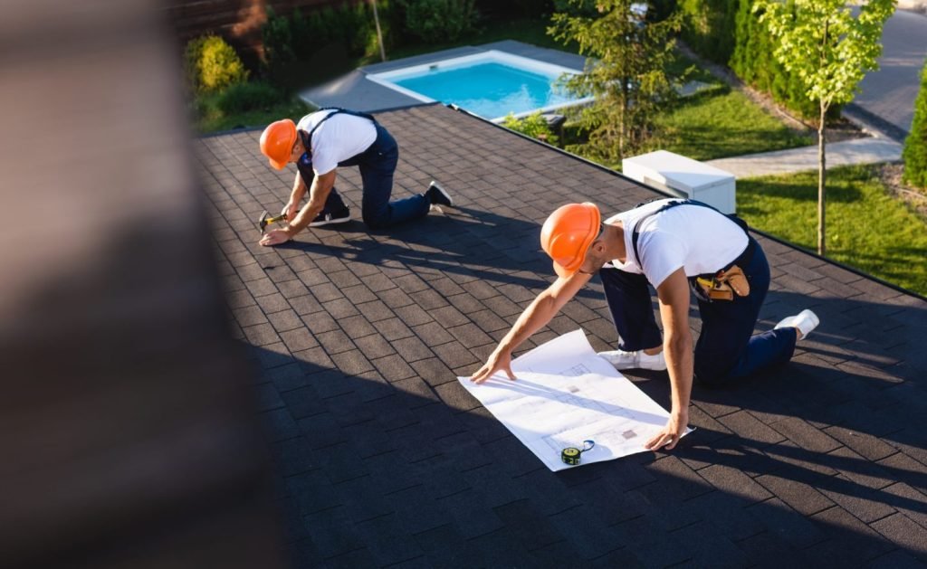 selective focus of builders with blueprint and tools working on roof of building